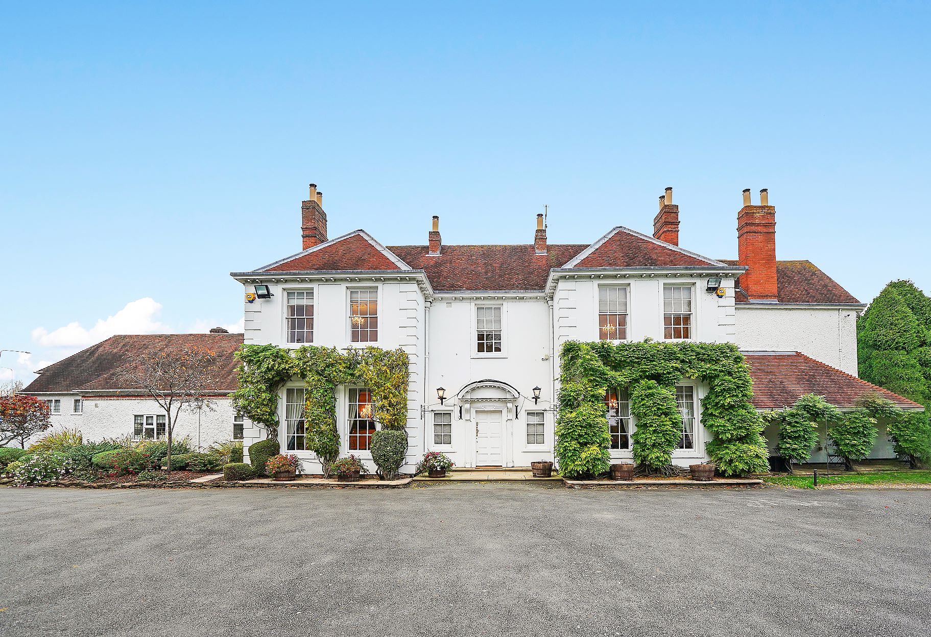 The white Georgian facade of Longbridge Manor with ivy-covered walls and red-brick chimneys.